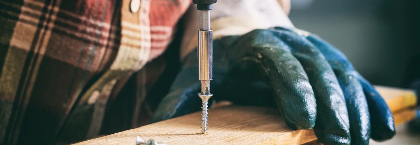 Person schraubt Holzbrett mit Akkuschrauber fest.